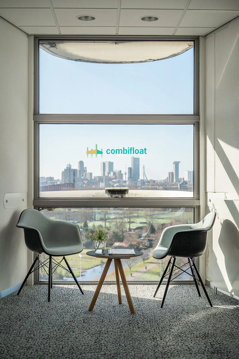 Twee moderne stoelen en een tafeltje staan bij een raam met uitzicht op de skyline van Rotterdam, in het kantoor van Combifloat in Rivium Quadrant.